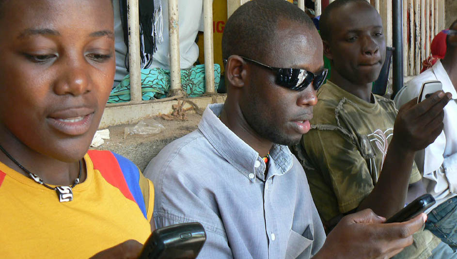 In Uganda, three people read text messages on their phones. Photo by Ken Banks