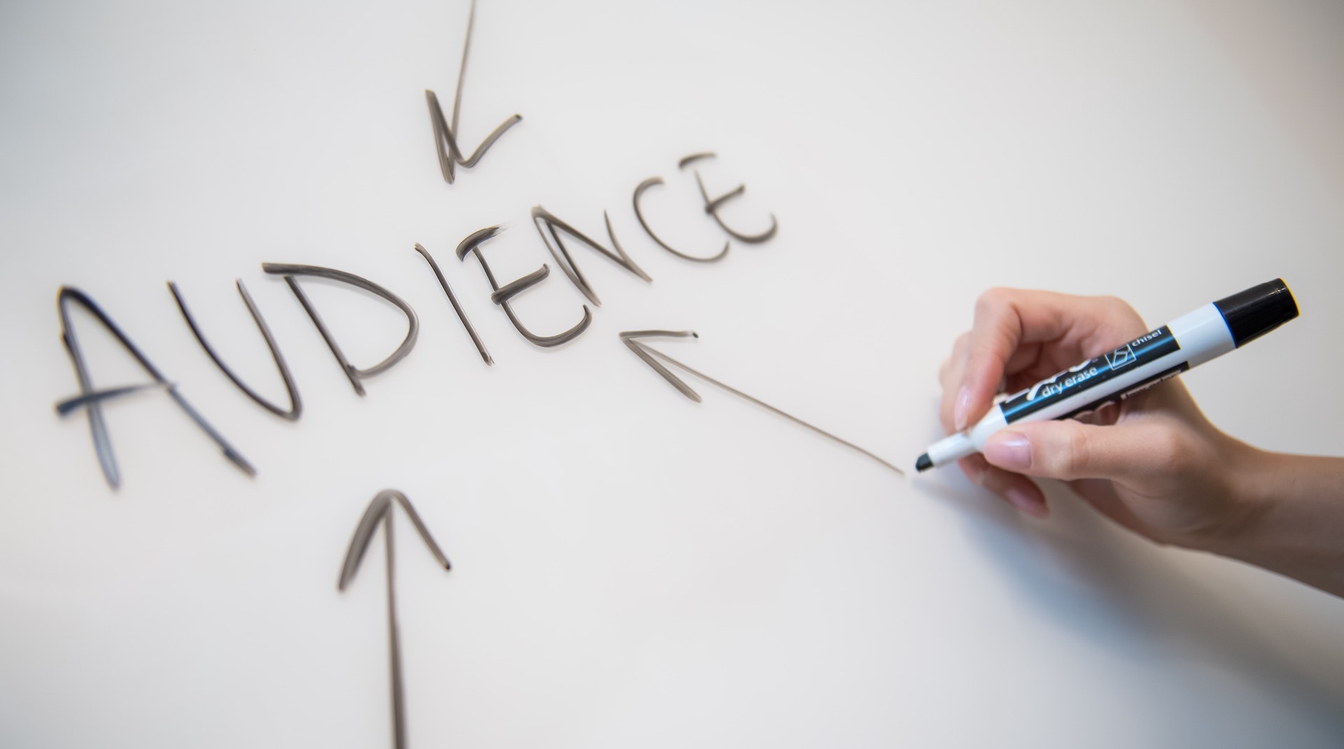 Someone writes an arrow pointing to the word audience on a whiteboard. Audience targeting and more focused metrics are important for subscription growth. Photo by Melanie Deziel from Unsplash.