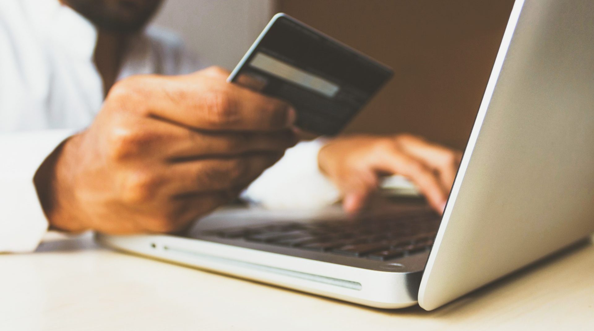 A person holds a credit card while making a purchase on a laptop. Photo by rupixen from Unsplash