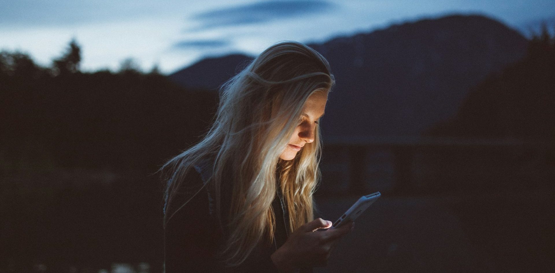 A woman looks at her mobile phone at dusk, the light of the screen illuminating her face. With the majority of many publishers' digital users coming from mobile, we look at how they can reorient their approach to mobile first.